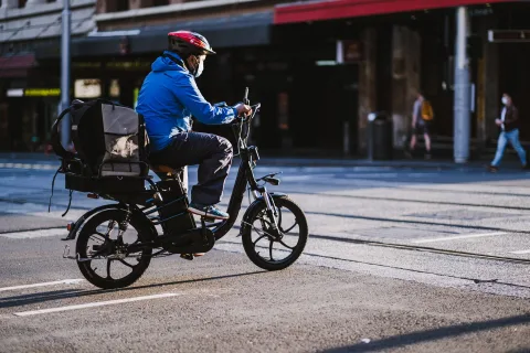 Une personne roule en ville sur un vélo à assistance électrique de couleur noire sous le soleil.