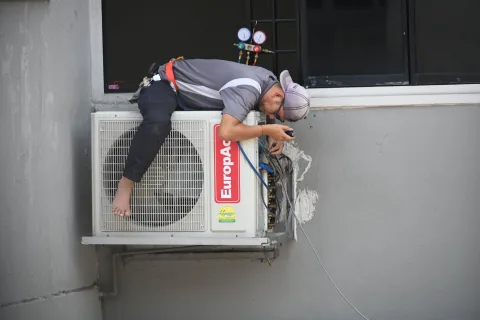 Un artisan installe une pompe à chaleur à l'extérieur d'une maison individuelle.