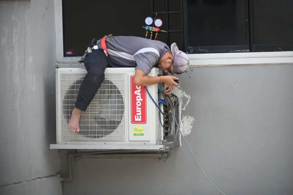 Un artisan installe une pompe à chaleur à l'extérieur d'une maison individuelle.