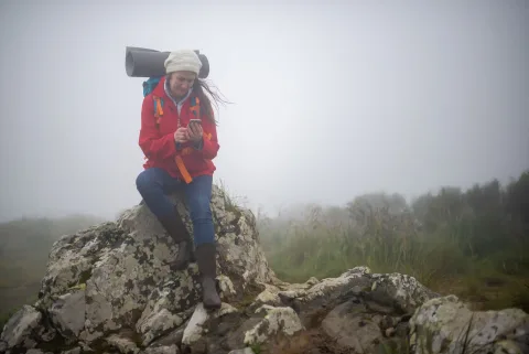 Un randonneur équipé d'un sac à dos consulte une application cartographique sur son smartphone au sommet d'une montagne.