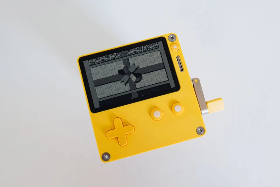 Une main tenant une console de retrogaming portable jaune avec un jeu de plateforme pixelise a l'ecran.