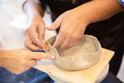 Une personne modèle un bol en argile autodurcissante blanche sur une table de cuisine en bois encombrée d'outils simples.