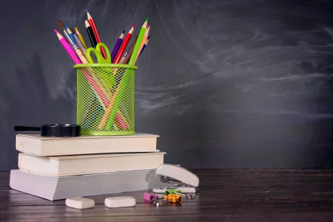 Une personne triant des crayons de couleur et des cahiers usagés sur un bureau en bois.