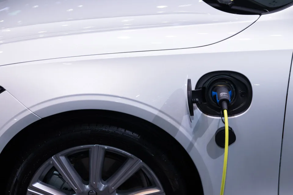 Une voiture électrique blanche branchée à une borne de recharge moderne en ville.