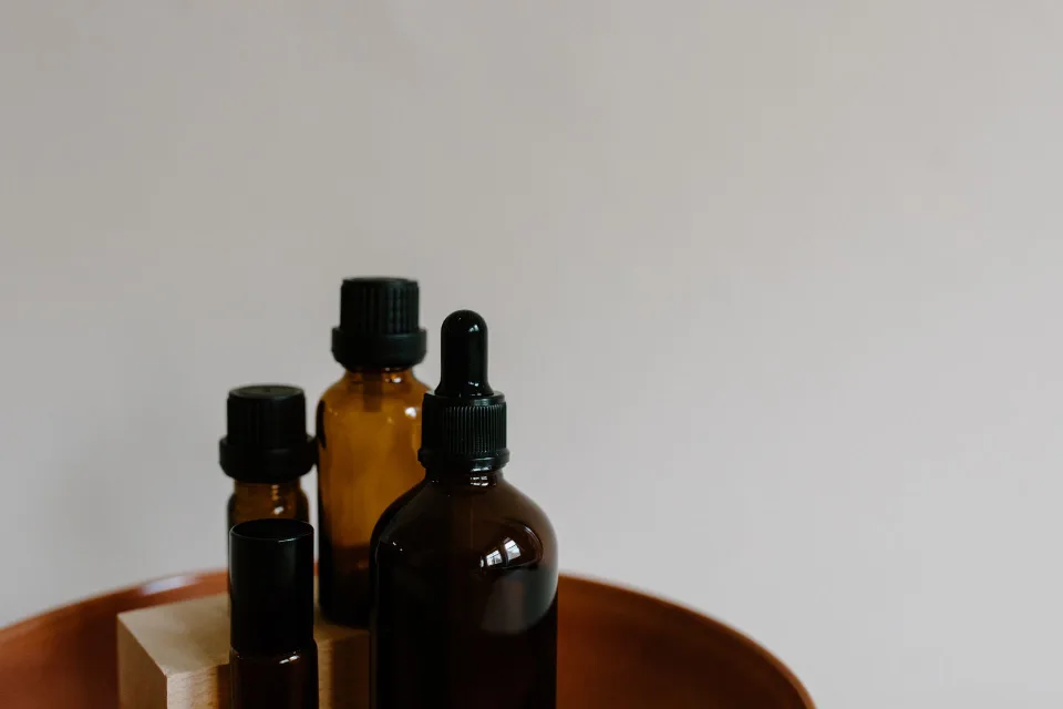 Un flacon d'huile essentielle de menthe poivrée posé à côté de disques de coton sur une table en bois.