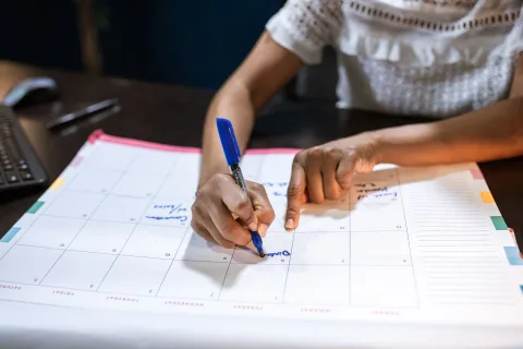 Une personne organise calmement sa semaine sur un carnet papier avec un stylo sur un bureau ensoleillé.