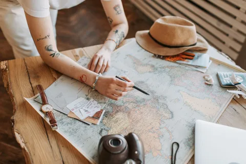 Une personne prépare son itinéraire de voyage sur un ordinateur portable avec une carte du monde en arrière-plan.