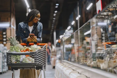 Une personne compare les prix des produits sur les étagères d'un supermarché avec sa liste.