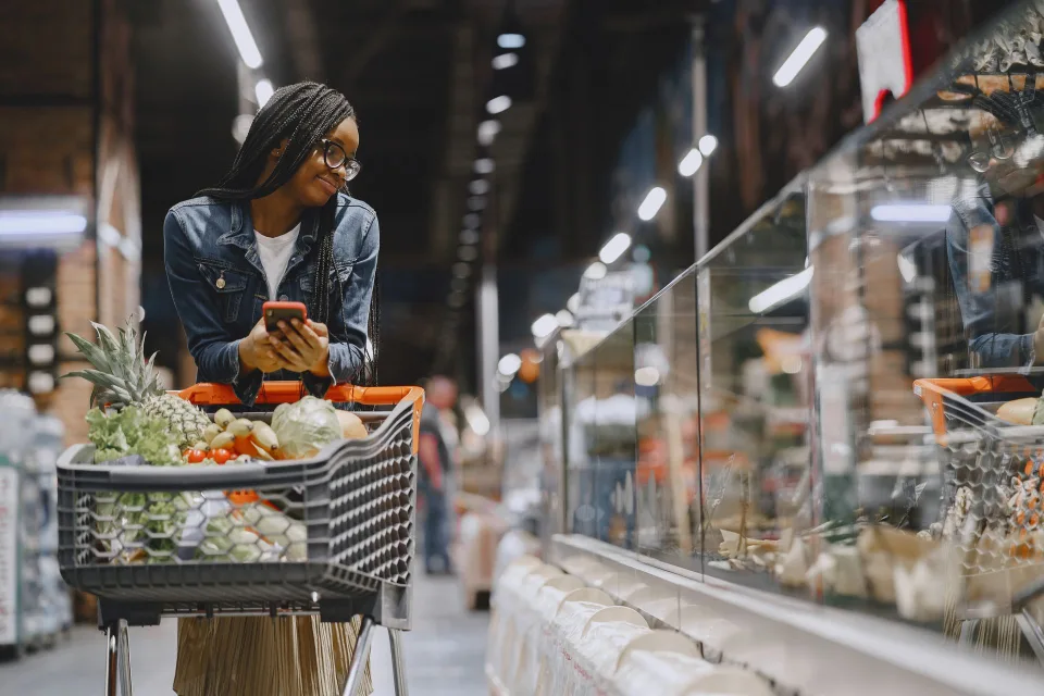 Une personne compare les prix des produits sur les étagères d'un supermarché avec sa liste.
