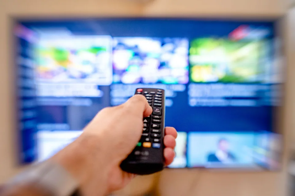 Une personne utilise sa télécommande devant un écran de télévision affichant plusieurs applications de streaming.