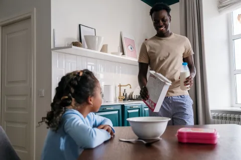 Une mère et son fils préparant joyeusement leur sac à dos dans une cuisine lumineuse.
