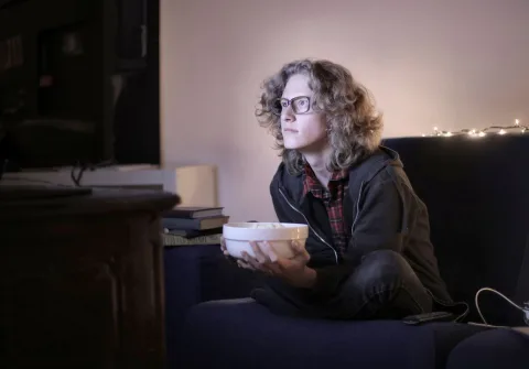 Une personne détendue sur un canapé regardant un film sur son écran de télévision avec du pop-corn.