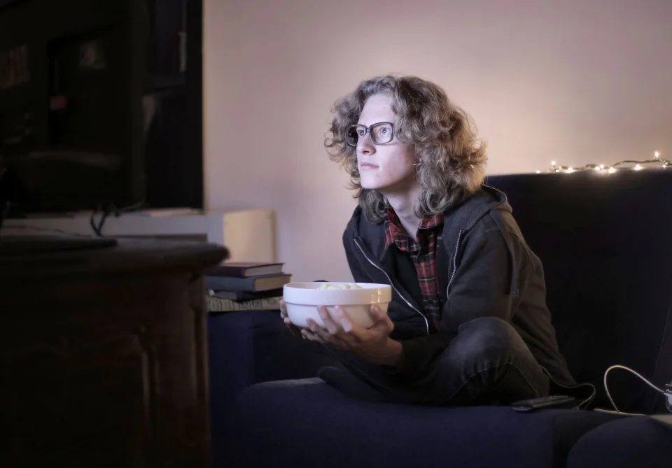 Une personne détendue sur un canapé regardant un film sur son écran de télévision avec du pop-corn.