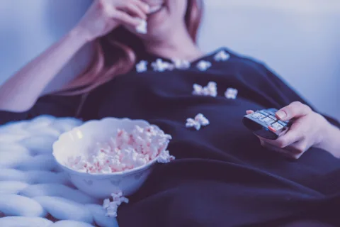 Une personne confortablement installée sur un canapé regarde un film sur son grand téléviseur dans un salon chaleureux.