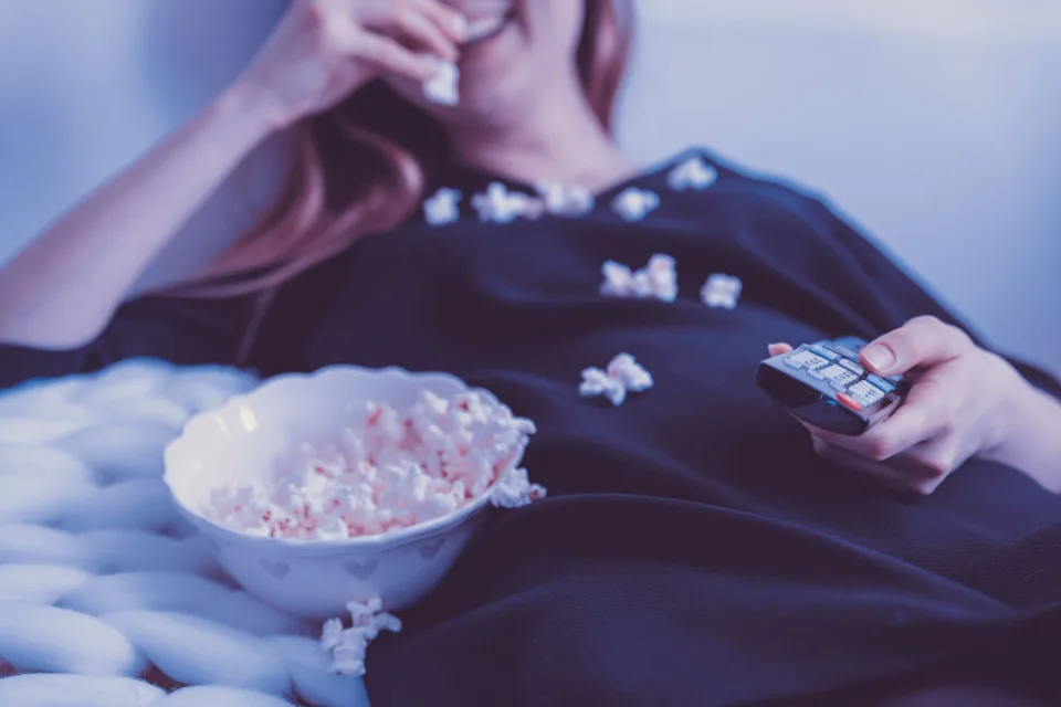 Une personne confortablement installée sur un canapé regarde un film sur son grand téléviseur dans un salon chaleureux.