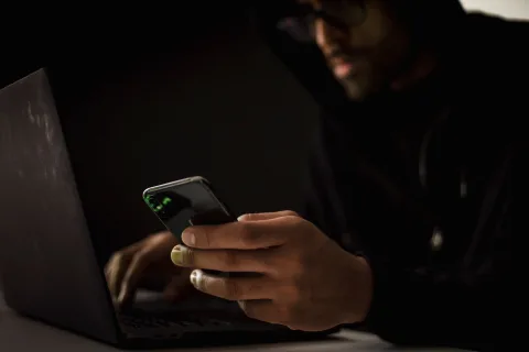 Une personne assise devant son ordinateur portable dans l'obscurité, analysant des données de sécurité à l'écran.