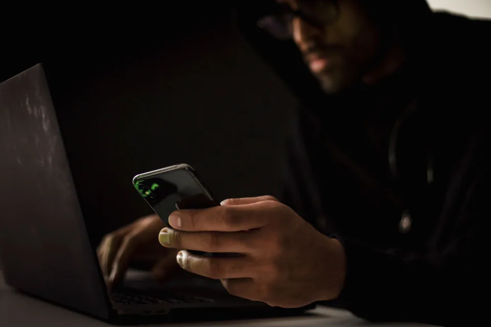 Une personne assise devant son ordinateur portable dans l'obscurité, analysant des données de sécurité à l'écran.