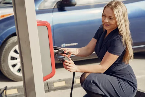 Une voiture électrique blanche branchée à une borne de recharge publique dans une rue urbaine.