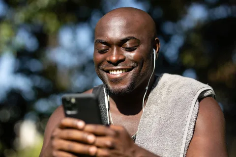Une personne de profil portant un casque audio sans fil de haute qualité et tenant son smartphone.
