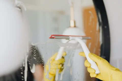 Une main appliquant une pâte de blanc de Meudon sur une surface vitrée avec un chiffon pour la faire briller.