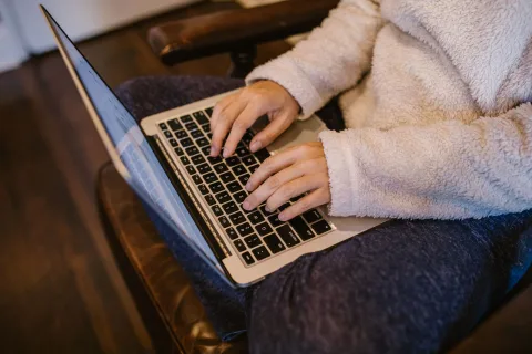 Une personne travaille sur un ordinateur portable dans un bureau chaleureux avec un plaid et un petit radiateur d'appoint.