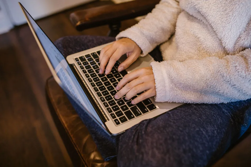 Une personne travaille sur un ordinateur portable dans un bureau chaleureux avec un plaid et un petit radiateur d'appoint.