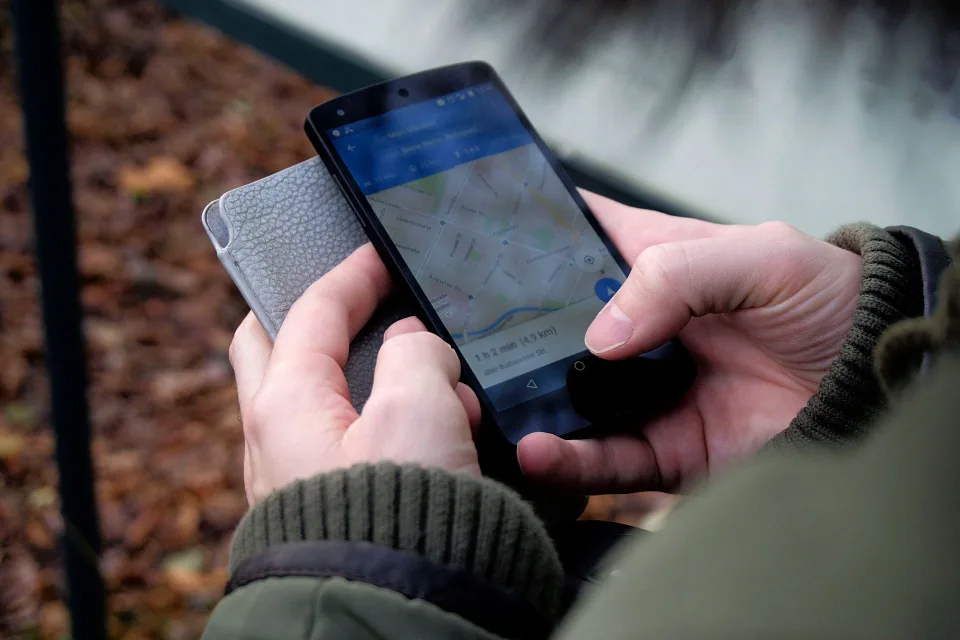 Une personne tient un smartphone affichant une carte de navigation routière hors ligne dans une rue animée à l'étranger.