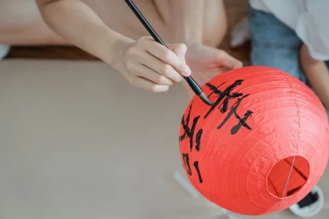 Une main peignant des motifs géométriques noirs sur un abat-jour boule en papier blanc.