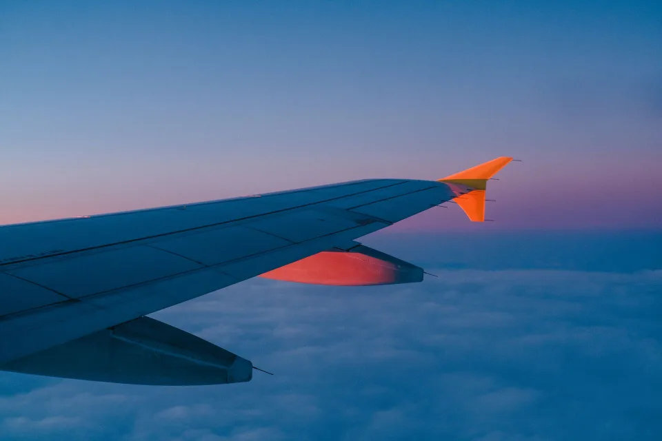 Aile d'un avion survolant des nuages au coucher du soleil, symbolisant le voyage aérien.