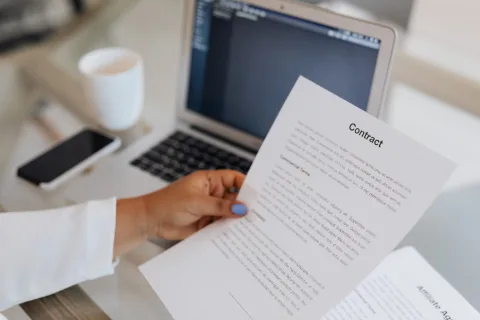 Une personne tape sur un clavier d'ordinateur avec plusieurs enveloppes et dossiers administratifs posés à côté du poste de travail.