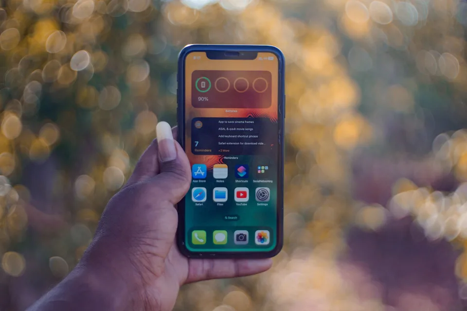 Une main tenant un smartphone moderne affichant l'interface de discussion de ChatGPT dans un jardin.
