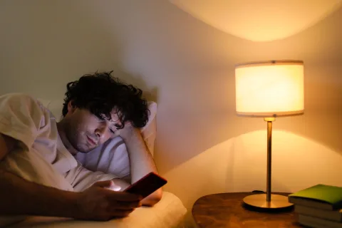 Une personne pose doucement son smartphone sur une table de chevet éteinte à côté d'une lampe tamisée