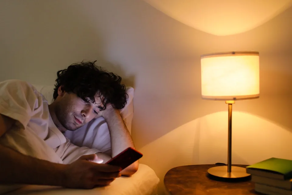 Une personne pose doucement son smartphone sur une table de chevet éteinte à côté d'une lampe tamisée