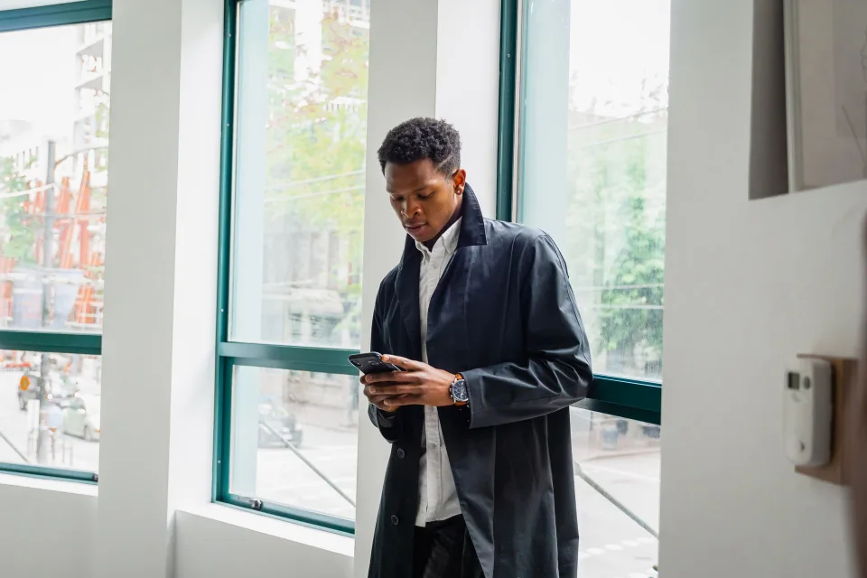 Une personne sous un parapluie consulte les prévisions sur son smartphone sous une pluie fine.