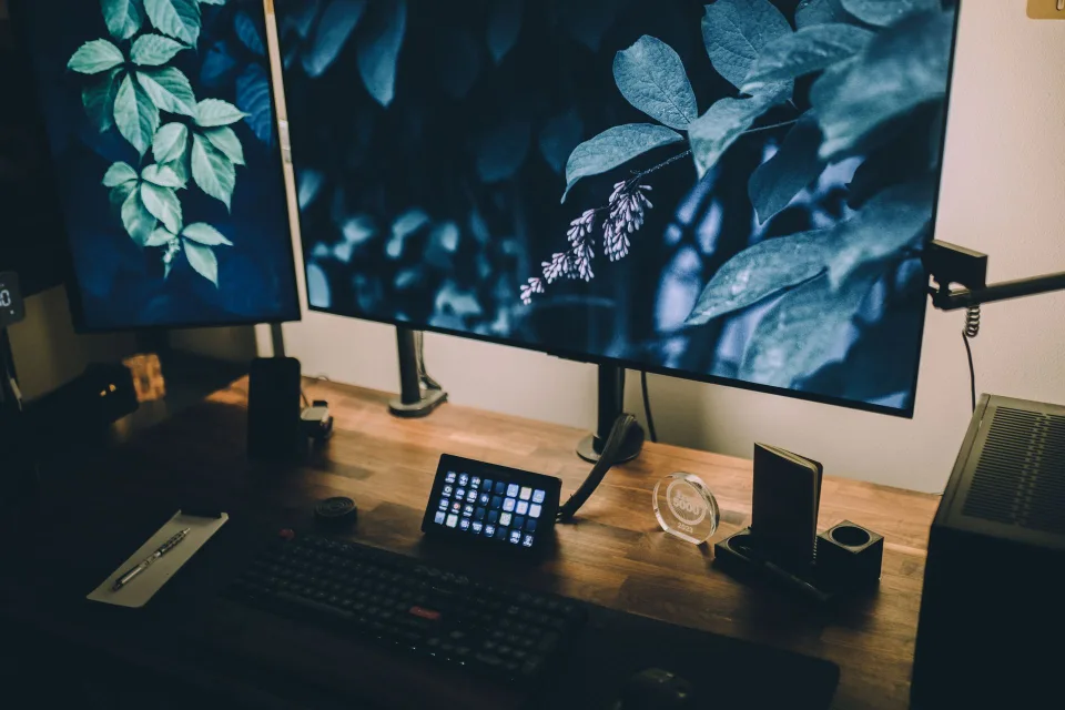 Un bureau de graphiste avec deux écrans affichant un logiciel de montage vidéo et une tablette graphique.