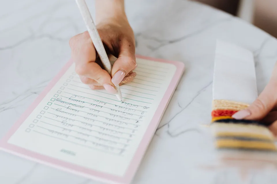 Une personne écrit une liste d'activités sur un carnet coloré dans un environnement calme avec des plantes.