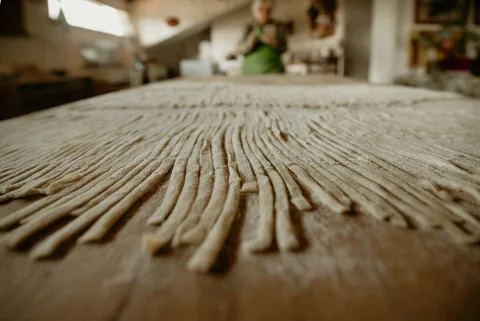 Une grand-mère italienne souriante prépare des pâtes fraîches maison dans sa cuisine lumineuse.