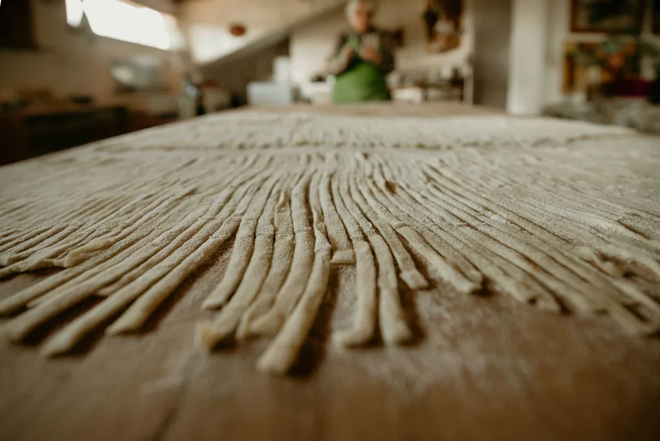 Une grand-mère italienne souriante prépare des pâtes fraîches maison dans sa cuisine lumineuse.
