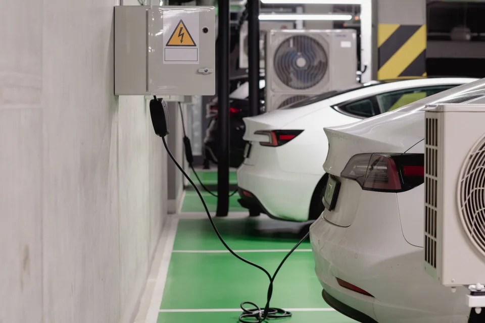 Une voiture électrique blanche branchée sur une borne de recharge murale dans un garage moderne.