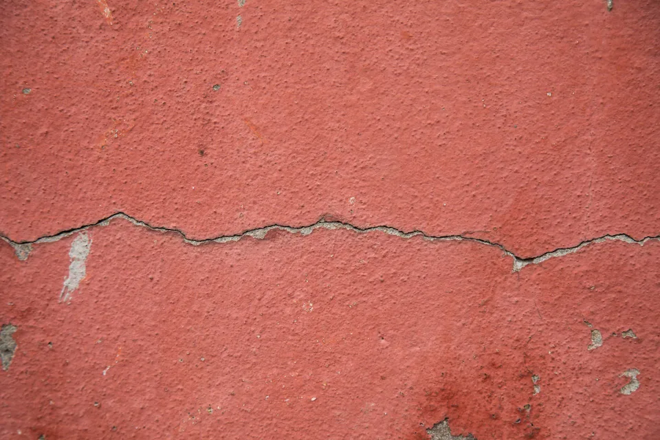 Une personne utilise un pistolet à mastic pour combler une fissure sur un mur en crépi beige.