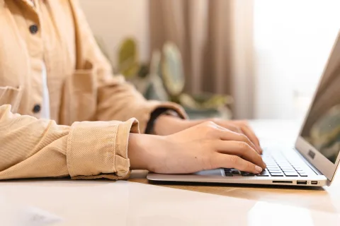 Une personne rédige un courrier officiel sur un ordinateur portable posé sur un bureau en bois.