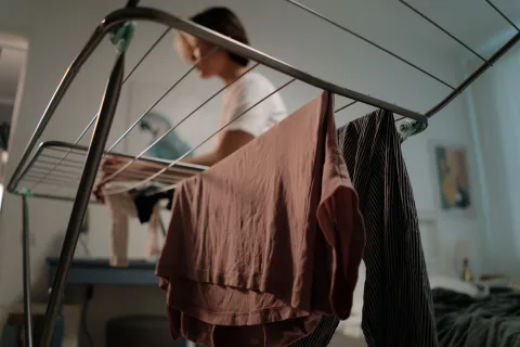 Un étendoir à linge rempli de vêtements propres disposé près d'une grande fenêtre éclairée.