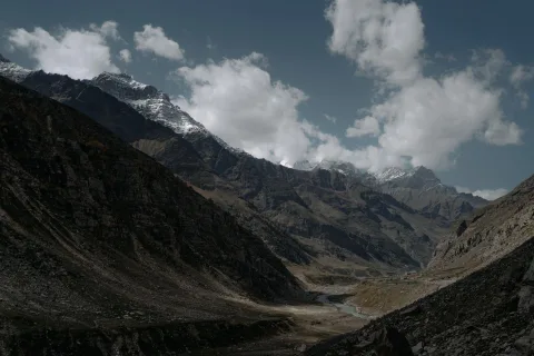 Une vallée verdoyante des Alpes du Nord avec un torrent au premier plan et des sommets enneigés.
