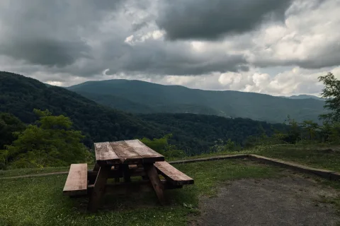 Un chapeau de cow-boy posé sur une table en bois face à un paysage de montagnes sauvages.
