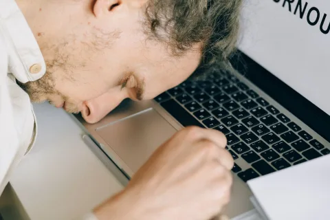Un homme en chemise dort paisiblement la tête posée sur ses bras croisés sur son bureau.