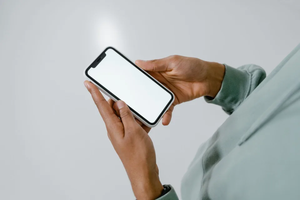 Une main tenant un smartphone contre un mur blanc pour détecter des vis cachées avec une application de magnétomètre.