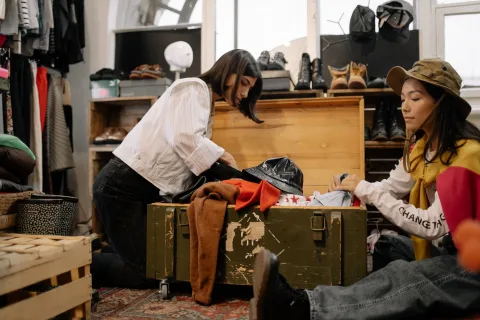 Une jeune femme examine attentivement les étiquettes de plusieurs vêtements suspendus sur un portant en bois.