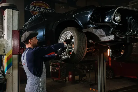 Un homme inspecte le moteur d'une voiture rouge des années quatre-vingt-dix ouverte dans un garage.