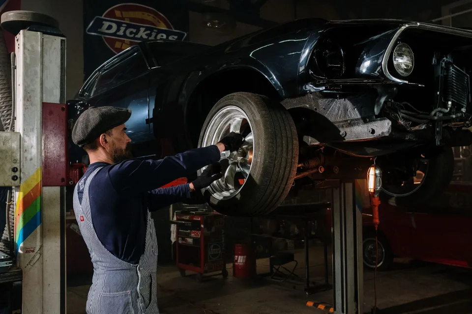 Un homme inspecte le moteur d'une voiture rouge des années quatre-vingt-dix ouverte dans un garage.