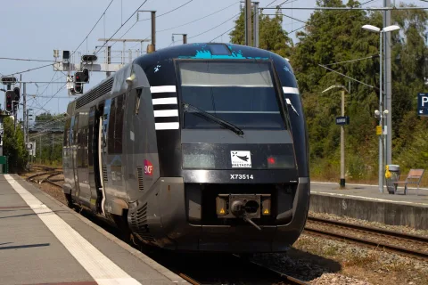 Vue depuis la fenêtre d'un train régional traversant la campagne française verdoyante.